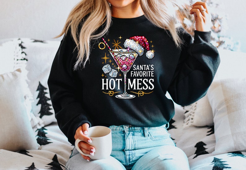 May include: A black sweatshirt with a festive design featuring a martini glass with a red liquid, ice cubes, and a Santa hat. The text "Santa's Favorite Hot Mess" is printed in gold lettering.