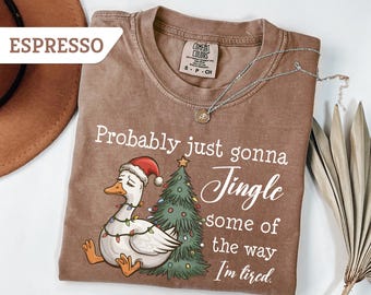 May include: Espresso-colored t-shirt with a graphic of a goose wearing a Santa hat and Christmas lights, next to a decorated Christmas tree. The text reads "Probably just gonna Jingle some of the way I'm tired."