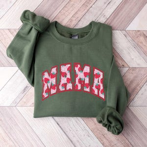 May include: A green sweatshirt with the word "MAMA" printed on the front in a white outline with a strawberry pattern inside the letters.