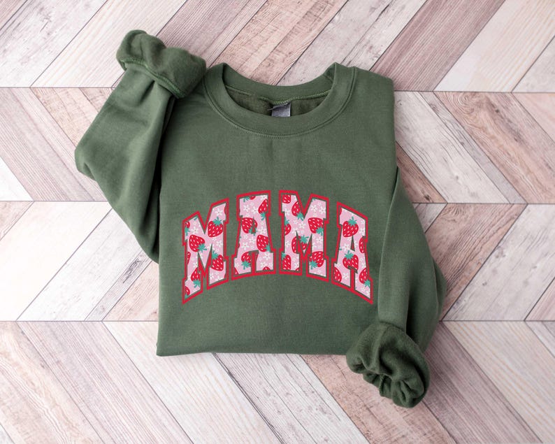 May include: A green sweatshirt with the word "MAMA" printed on the front in a white outline with a strawberry pattern inside the letters.