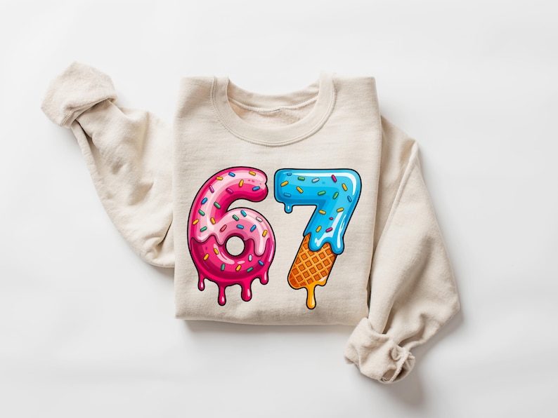 May include: Beige sweatshirt with a colorful graphic of the number 67. The number 6 is designed as a pink donut with sprinkles, and the number 7 is designed as blue ice cream melting over a waffle cone.
