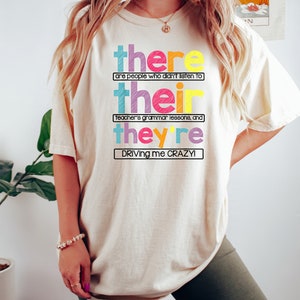Puede incluir: Camiseta color crema con el texto "there are people who didn't listen to their teacher's grammar lessons, and they're driving me CRAZY!" en letras de colores. La camiseta es de estilo casual.
