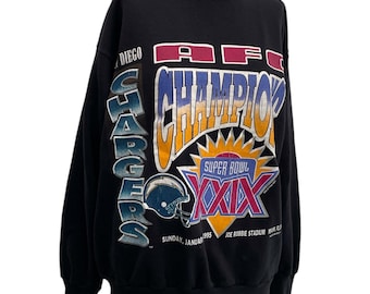 Puede incluir: Sudadera negra con un diseño gráfico. El diseño incluye el texto "AFC CHAMPIONS" y "SUPER BOWL XXIX", un casco de fútbol americano y las palabras "SAN DIEGO CHARGERS". La sudadera es de 1995.