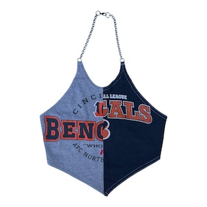 May include: A split-design halter top featuring a grey left side and a black right side. The front displays the text CINCINNATI BENGALS, AFC NORTH, and WHO DEY in orange and white lettering. The garment is held by a silver-toned metal chain strap.
