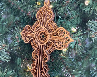 May include: A wooden cross ornament with intricate laser-cut details. The cross is a light brown color and has a circular design in the center.