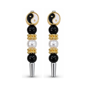 May include: A pair of dangle earrings featuring a circular yin yang charm at the top, followed by a black bead, a gold-toned textured spacer, a white pearl-like bead, another gold-toned spacer, a black bead, and a silver-toned conical base.
