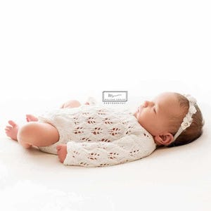 Könnte beinhalten: Ein neugeborenes Baby trägt ein weißes Häkel-Outfit mit langen Ärmeln und ein Stirnband mit weißen Blumen. Das Baby liegt auf einer weißen Oberfläche.