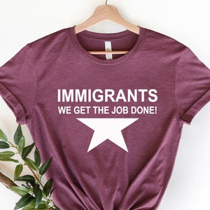 May include: A maroon t-shirt with white text that reads 'Immigrants We Get The Job Done!' and a white star below the text.