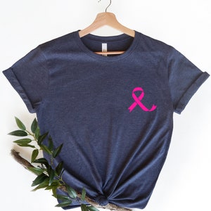 K&ouml;nnte beinhalten: Ein dunkelblaues T-Shirt mit einem rosa Band auf der Vorderseite. Das Band ist ein Symbol f&uuml;r die Sensibilisierung f&uuml;r Brustkrebs.