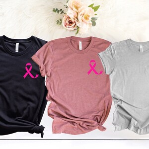 K&ouml;nnte beinhalten: Drei T-Shirts mit einem rosa Band-Design. Die Shirts sind schwarz, rosa und grau.