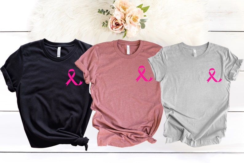 K&ouml;nnte beinhalten: Drei T-Shirts mit einem rosa Band-Design. Die Shirts sind schwarz, rosa und grau.