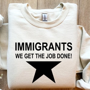 May include: A beige sweatshirt with the text "Immigrants We Get The Job Done!" and a black star printed on the front.