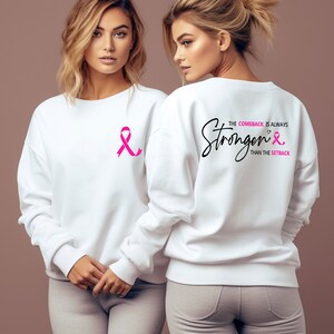 K&ouml;nnte beinhalten: Wei&szlig;er Pullover mit einem rosa Band auf der Vorderseite und dem Text "The comeback is always stronger than the setback" mit einem rosa Band auf der R&uuml;ckseite.