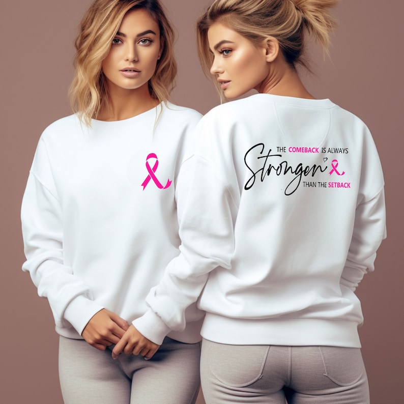 K&ouml;nnte beinhalten: Wei&szlig;er Pullover mit einem rosa Band auf der Vorderseite und dem Text "The comeback is always stronger than the setback" mit einem rosa Band auf der R&uuml;ckseite.
