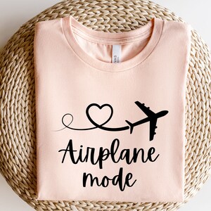 May include: A peach-colored t-shirt with a black airplane graphic and the text "Airplane mode" in a cursive font.