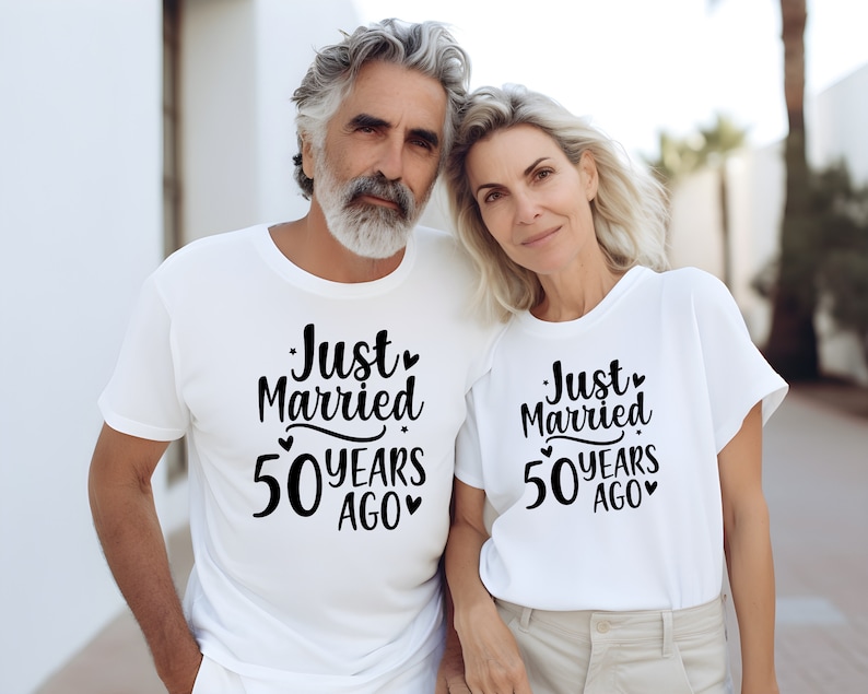 May include: A couple wearing white t-shirts with the text "Just Married 50 Years Ago" printed on them. The couple are standing close together and smiling.