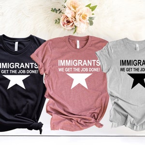May include: Three t-shirts with the text "Immigrants We Get The Job Done!" and a white star on a black shirt, a white star on a pink shirt, and a black star on a gray shirt.