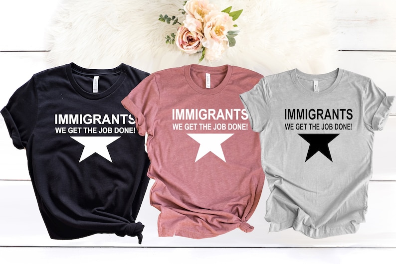 May include: Three t-shirts with the text "Immigrants We Get The Job Done!" and a white star on a black shirt, a white star on a pink shirt, and a black star on a gray shirt.