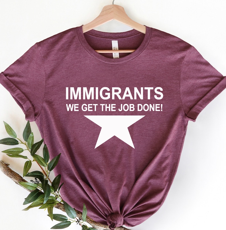 May include: A maroon t-shirt with white text that reads 'Immigrants We Get The Job Done!' and a white star below the text.