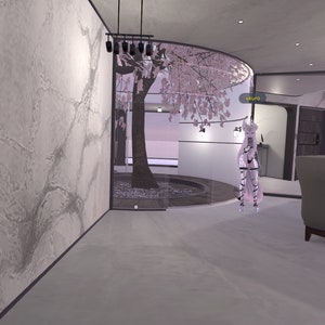 May include: A white room with a cherry blossom tree in a glass enclosure. The room has a grey sofa and a white figure standing in the middle of the room. The text "GRLITO" is visible on a wall.
