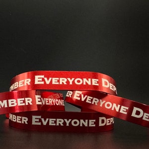 May include: Red wristbands with the text "REMEMBER EVERYONE DEPLOYED" in white. The bands are slightly curved and overlapping, with a reflective surface. The background is a solid black.