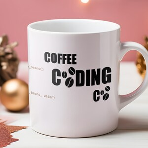 K&ouml;nnte beinhalten: Wei&szlig;e Keramik-Kaffeetasse mit schwarzem Text, der "COFFEE CODING C#" mit Kaffeekorn-Symbolen lautet. Die Tasse steht auf einer wei&szlig;en Oberfl&auml;che mit rosa Hintergrund.