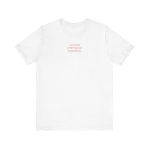 May include: A white t-shirt with the words "essential professional empathetic" printed in a soft pink color. The shirt has short sleeves and a crew neck.