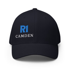 May include: A navy blue baseball cap with a white embroidered logo that says "RI CAMDEN" and a blue "RI" logo.