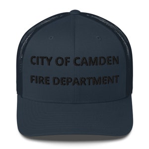 May include: A navy blue trucker hat with a black mesh back. The front of the hat has the text "CITY OF CAMDEN FIRE DEPARTMENT" embroidered in black.