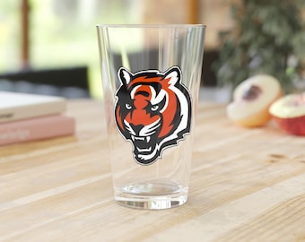 Könnte beinhalten: Ein klares Glas Pint-Glas mit einem schwarzen und orangefarbenen Tigerkopf-Logo. Der Tiger hat einen weißen Streifen auf der Stirn und eine schwarze Nase.