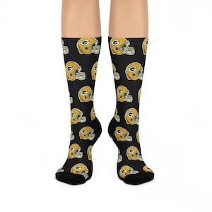 Puede incluir: Un par de calcetines negros con un patrón repetido de cascos de fútbol amarillo y verde.