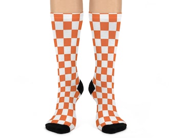 May include: A pair of knee-high socks with a checkered pattern in orange and white. The socks have black heels and toes, and are displayed against a white background.