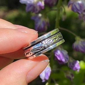 May include: A silver spinning ring with a floral design. The ring is made of multiple bands that spin around each other.