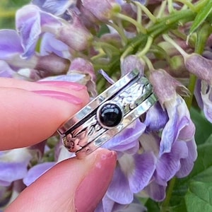 May include: A silver spinning ring with a black gemstone set in the centre. The ring is decorated with floral designs and has a hammered finish.