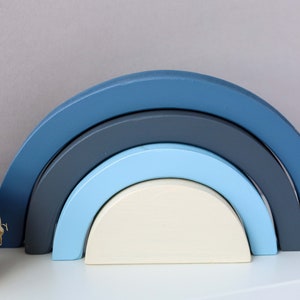 May include: A set of five wooden rainbow arches in shades of blue and white. The arches are stacked on top of each other, creating a colourful and playful design.