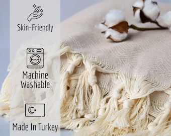 May include: Cream-colored woven textile with knotted fringe. The image shows a close-up of the fabric, with a sprig of cotton blossoms in the background. The text on the left side of the image says "Skin-Friendly", "Machine Washable", and "Made In Turkey".