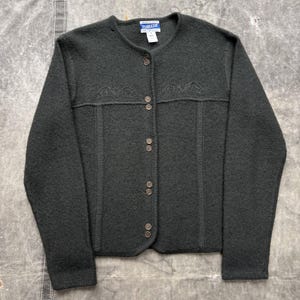 May include: Dark green button-up cardigan with a round neckline. The sweater features decorative stitching across the chest and is made of a textured fabric. The label reads "Pendleton".