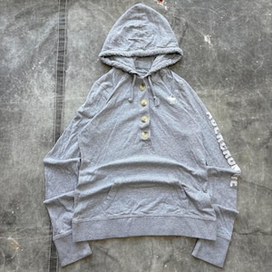 May include: A grey hooded sweatshirt with a kangaroo pocket and a button-up neckline. The sweatshirt has long sleeves with the brand name printed on the left sleeve. The brand's logo is embroidered on the chest.