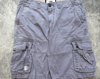May include: Gray cargo shorts with multiple pockets and a button closure. The shorts have a faded appearance and the brand name "garga" is visible on the waistband. The shorts are made of a durable fabric.