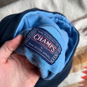 May include: A blue and navy blue hoodie with a white tag that reads "Made Exclusively for Champs Sports by Team Edition Apparel".
