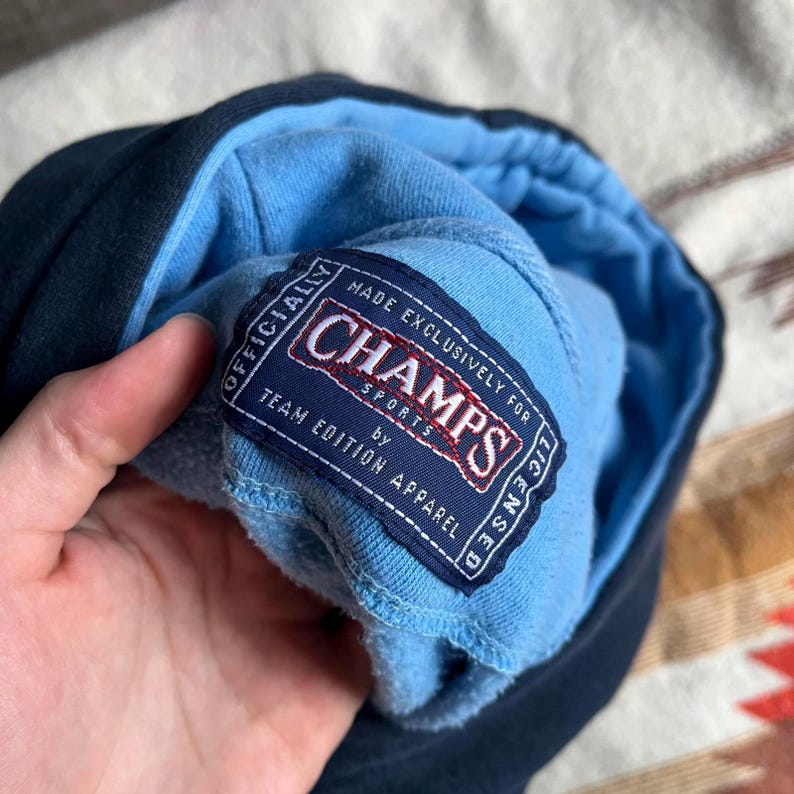 May include: A blue and navy blue hoodie with a white tag that reads "Made Exclusively for Champs Sports by Team Edition Apparel".