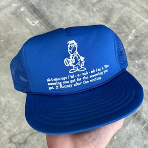 May include: A blue trucker hat with a white cartoon graphic and text. The text reads "al-i-mo-ny: /'al-ə-mō-nē/ n; 1. The screwing you get for the screwing you got. 2. Bounty after the mutiny."