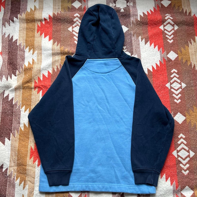 May include: A blue and navy blue hooded sweatshirt with a raglan sleeve design. The sweatshirt has a light blue body and navy blue sleeves and hood.