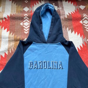 May include: A blue and navy blue hooded sweatshirt with the word "CAROLINA" in white lettering on the front.