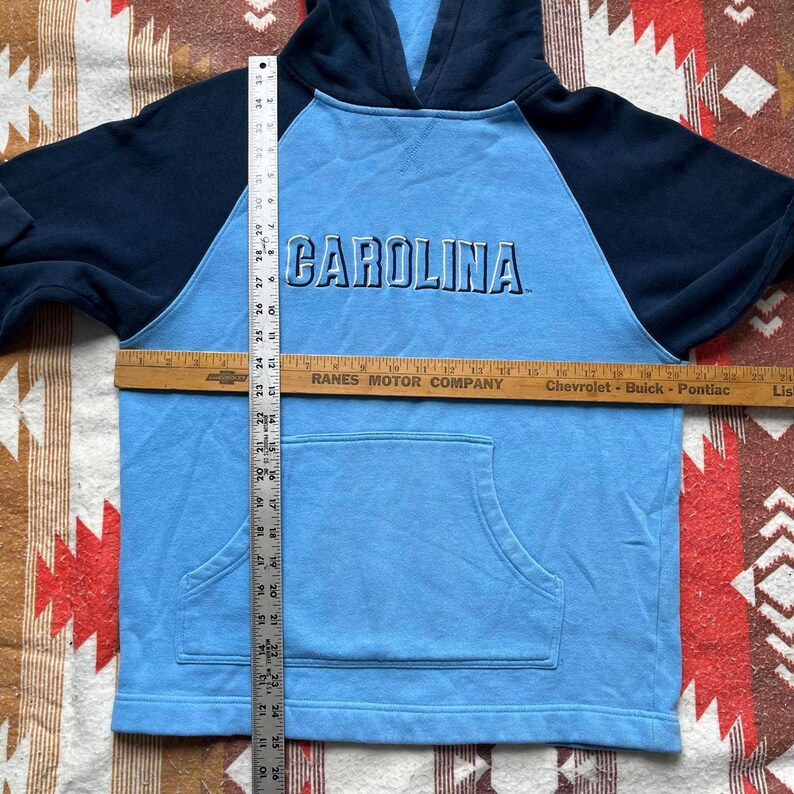 May include: A light blue hooded sweatshirt with navy blue sleeves. The sweatshirt has a large "CAROLINA" graphic on the front.