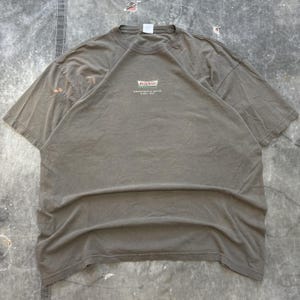 May include: A faded olive green t-shirt featuring the Krispy Kreme logo in red, white, and green. The text "Doughnuts & Coffee Since 1937" is printed below the logo. The shirt has a crew neck and short sleeves.