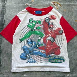Könnte beinhalten: Weißes T-Shirt mit roten Ärmeln und Kragen mit Power Rangers Time Force-Charakteren in Grün, Rot und Blau. Das Shirt hat ein grafisches Design mit dem Power Rangers Time Force-Logo.