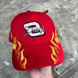 Może przedstawiać: Czerwona czapka bejsbolówka z haftowanym białym numerem 8 i tekstem "Dale Jr."  Czapka ma haftowane żółte płomienie po bokach.