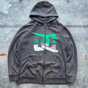 May include: A gray zip-up hoodie with a green and white DC logo on the front.