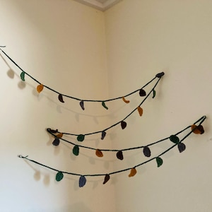 May include: Three strands of crocheted leaf garland in green, purple, and orange hanging on a white wall.
